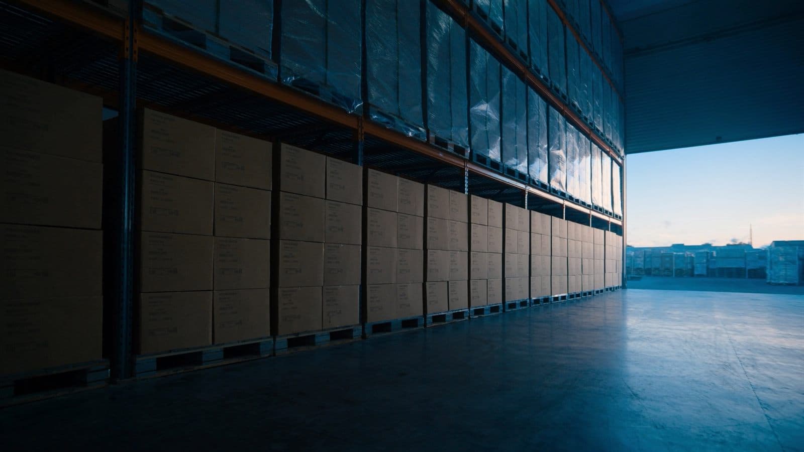 Pallets of plain cartons on racking in a distribution warehouse at dawn